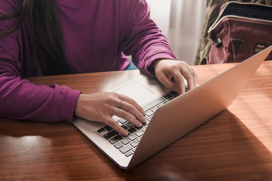 Young woman wearing a purple sweater using her computer for study at her desk. Remote work. - Powered by Adobe
