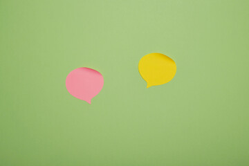 Pink and yellow paper speech bubbles on green background, minimal dialogue communication concept