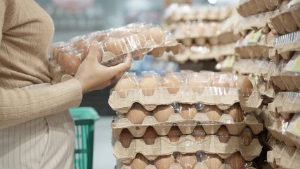 A woman is holding a carton of eggs. The carton is in a store. There are many cartons of eggs in the store