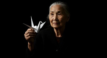 Elderly Woman Holding a Delicate Paper Crane Against a Dark Background