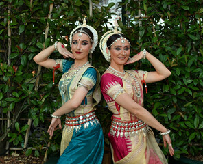 Two beautiful girls dancers in traditional Indian clothes in the park outdoors against the background of greenery in a dance pose