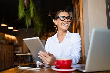 Smiling Woman Using Tablet and Laptop at Cafe with Coffee Cup