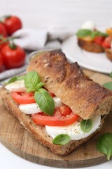 Tasty sandwich with mozzarella cheese, tomatoes and basil on white wooden table, closeup