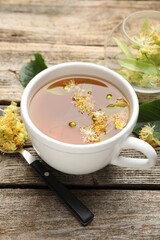 Tasty linden tea in cup, spoon, leaves and flowers on wooden table, closeup