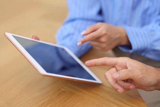 Business partners working with tablet at wooden table, closeup