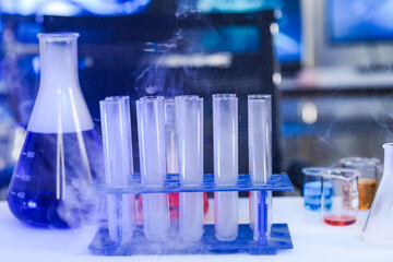 Scientific experiment in a high-tech lab. Test tubes with a smoking chemical reaction on a bench with flasks, beakers, and computer screens displaying DNA data in the background.