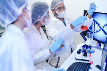 A team of scientists in a modern laboratory meticulously works on an experiment, pipetting a red...