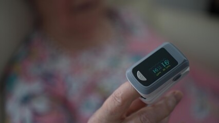 Closeup of an oximeter displaying oxygen levels on the finger of a senior woman in a care facility, highlighting health monitoring in aged care.