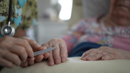 Nurse gently files the nails of an elderly woman, promoting comfort and care during a visit. The...
