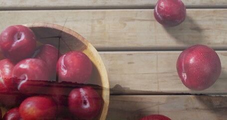 Displaying wooden bowl holding red plums on rustic tabletop, with scattered plums, copy space