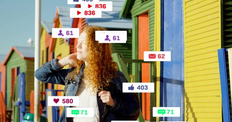 Standing redhead wearing denim jacket and backpack on boardwalk, with floating social media icons