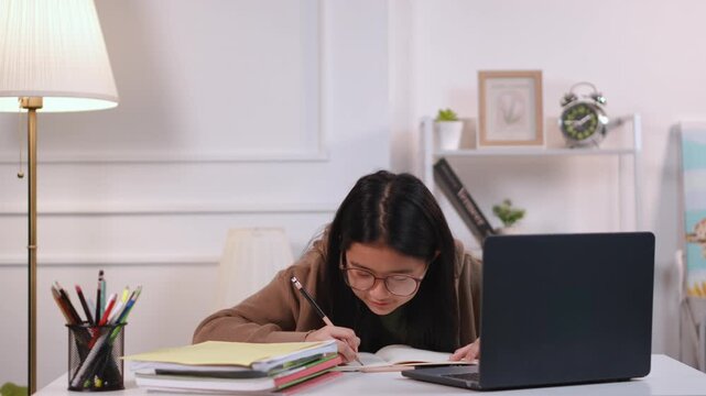 Asian girl typing on computer and taking notes during online class