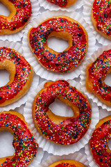 Top view flat lay of delicious donuts with red glaze and colorful sprinkles on a white plate, a...