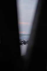 Ocean View Through Narrow Gap with Rocky Shoreline and Cloudy Pink Sky in a Dramatic Natural Scene
