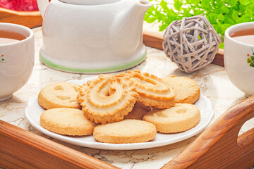 Danish butter cookies on white plate with tea on wooden tray.