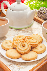 Danish butter cookies on white plate with tea on wooden tray.