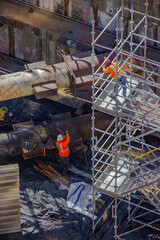 Construction workers inspecting scaffolding and metal pipes at urban infrastructure site