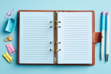 Open notebook with blank pages surrounded by colorful stationery on a blue background