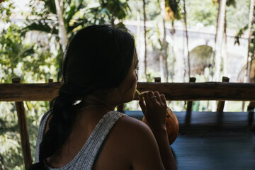 Tourist savoring refreshing coconut water while soaking in the serene view of the Nine Arch Bridge and lush tropical jungle in Ella, Sri Lanka