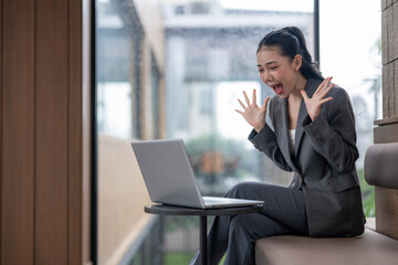 Excited businesswoman celebrating success while using laptop in office lobby