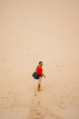 Man standing at bottom of sand dune at the beach looking back over his shoulder