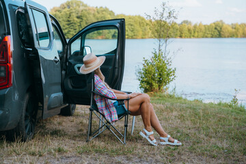 Van life moment. Woman by a lake next to her campervan, soaking in solitude and nature’s beauty.