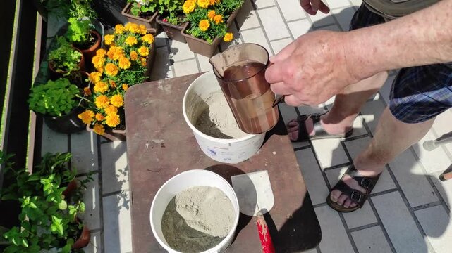 An elderly man is stirring cement in a bucket, by adding water to it he makes it more liquid, hand-held shot
