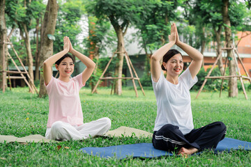 Two women practice yoga outdoors on a sunny day They are sitting on yoga mats in nature