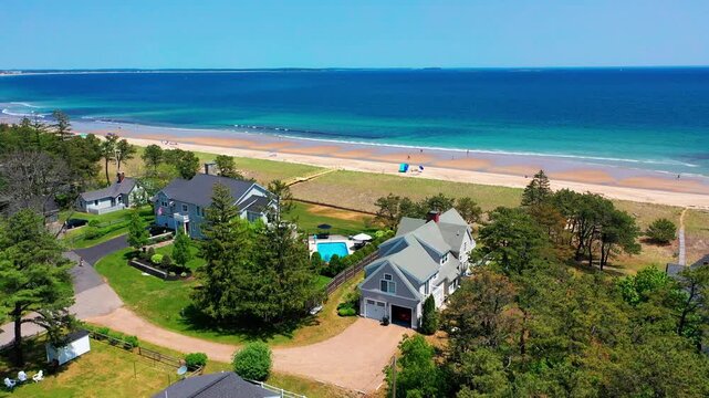 Aerial drone view of a peaceful Maine beach house. Oceanfront yard, deck, patio, and big windows create the perfect vacation getaway and prime real estate near the Atlantic shore.