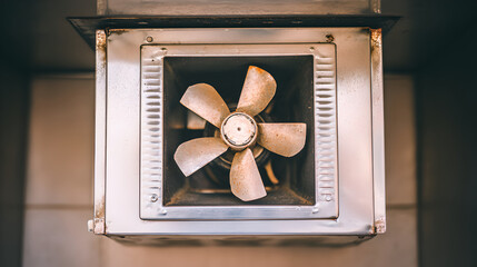 A five-blade exhaust fan rotating inside a dark, metallic circular ventilation shaft, creating a tunnel effect.
