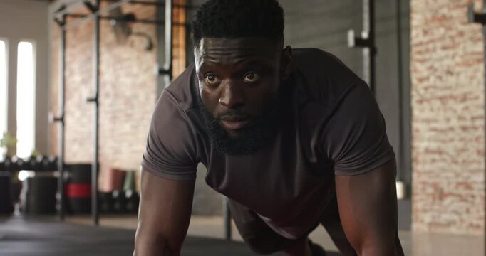 Positioning into plank, African American man in gear doing pushups on mat in gym for strength