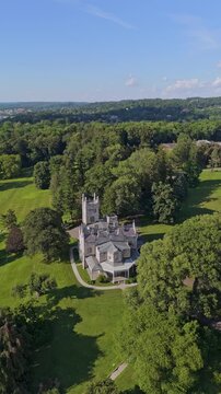 Aerial orbit of Lyndhurst Mansion surrounded by trees in Tarrytown, New York. Reveal shot of Governor Mario M. Cuomo Bridge in background