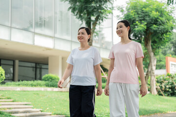 Two women enjoy a leisurely walk through a green park smiling and appreciating the outdoors