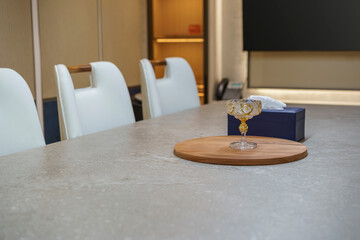 Close-up of a luxury meeting room table. An ornate gilded glass sits on a wooden tray next to a...