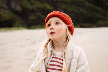 Child girl walking outdoor on the beach kid portrait blonde hair 5 years old in red hat family travel vacations autumn season