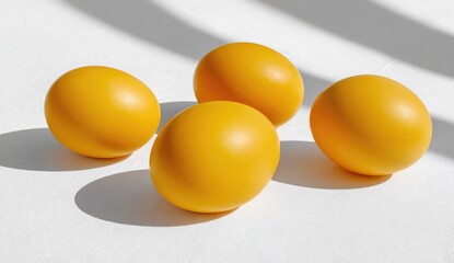 Four vibrant yellow eggs on a white surface with shadows
