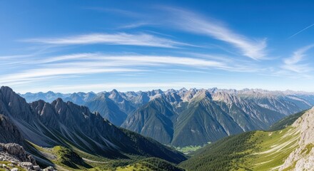 A panoramic view of a mountain range with jagged peaks and lush green valleys under a clear blue sky with wispy clouds.
