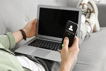 Handsome man with laptop using blank mobile phone on sofa at home, closeup