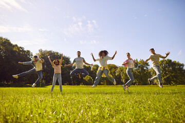 Group of a young people friends jumping in a row in the summer park. Happy diverse people girls and boys having fun outdoors. Smiling students in casual clothes spending time together.