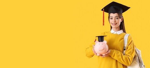 Female student in graduation hat holding piggy bank on yellow background with space for text....