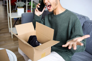Frustrated Young Asian Man On The Phone, Expressing Disbelief With Open Box Of Shoes