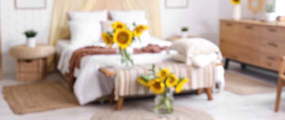 Blurred view of light bedroom with cozy bed and beautiful sunflowers