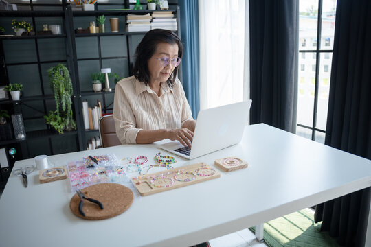 Mature asian woman business laptop E-commerce entrepreneurship owner preparing jewellery accessories handcraft.