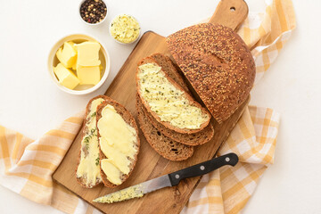 Wooden board of bread slices with fresh butter and bowl of peppercorn on white background