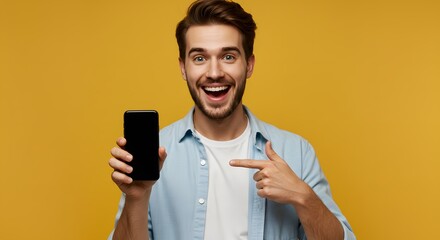 Excited young man holding and pointing at a smartphone, showcasing technology and communication with a happy, positive expression against a vibrant yellow background