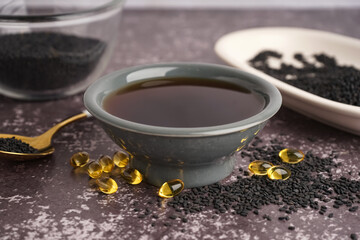 Bowl of oil with spoon, capsules and sesame seeds on grey grunge background