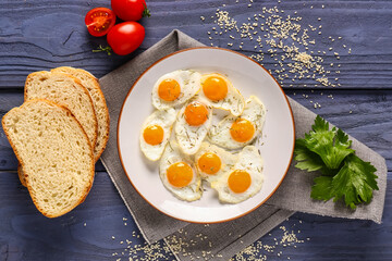 Plate with fried quail eggs, parsley and tomatoes on blue wooden background