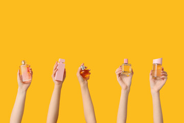 Female hands with different pink bottles of perfume on yellow background