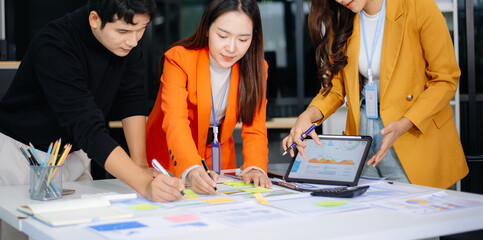 Young Asian business team brainstorming with data charts, tablet, and sticky notes. Perfect for teamwork, corporate planning, and startup