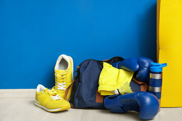 Fototapeta premium Boxing gloves, sneakers, yoga mat, sports bag and water bottle on floor near blue wall